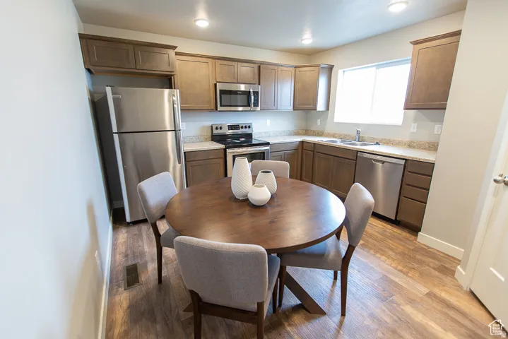 Kitchen featuring stainless steel appliances, wood-finish flooring, recessed lighting, a double basin sink, and a window
