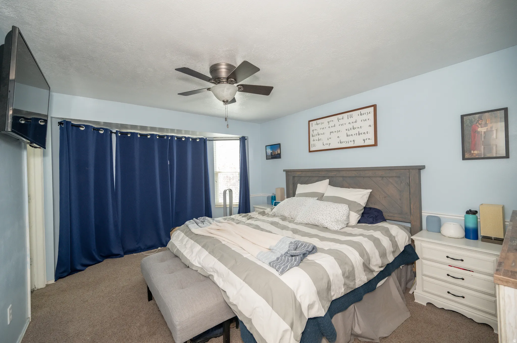 Carpeted room featuring light blue walls, a ceiling fan with light fixture, and a window with dark blue curtains