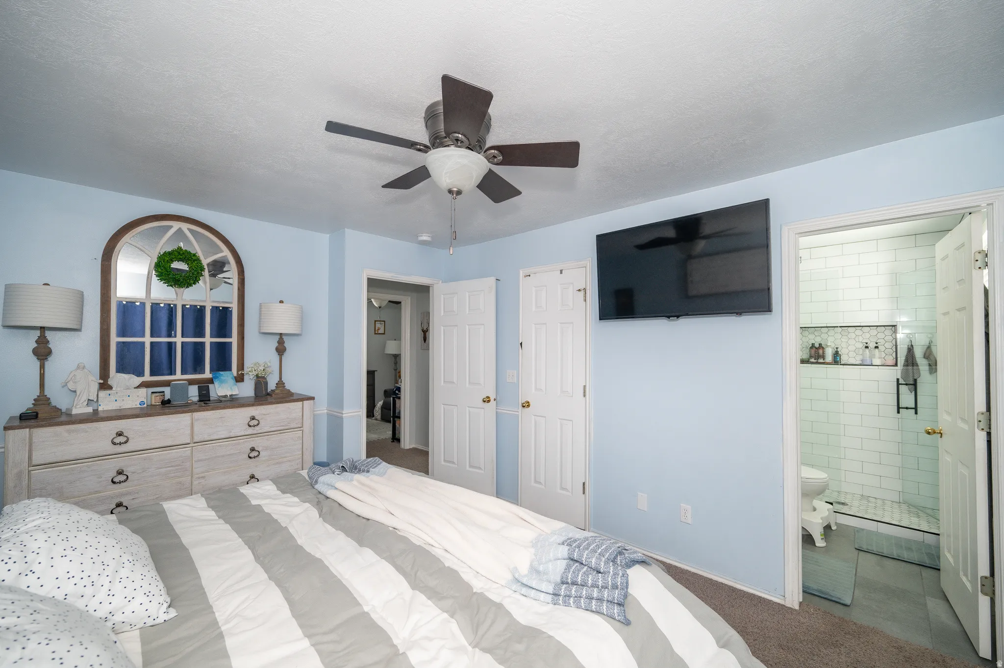 Bedroom featuring a ceiling fan, arched window with white trim, and a wall-mounted television