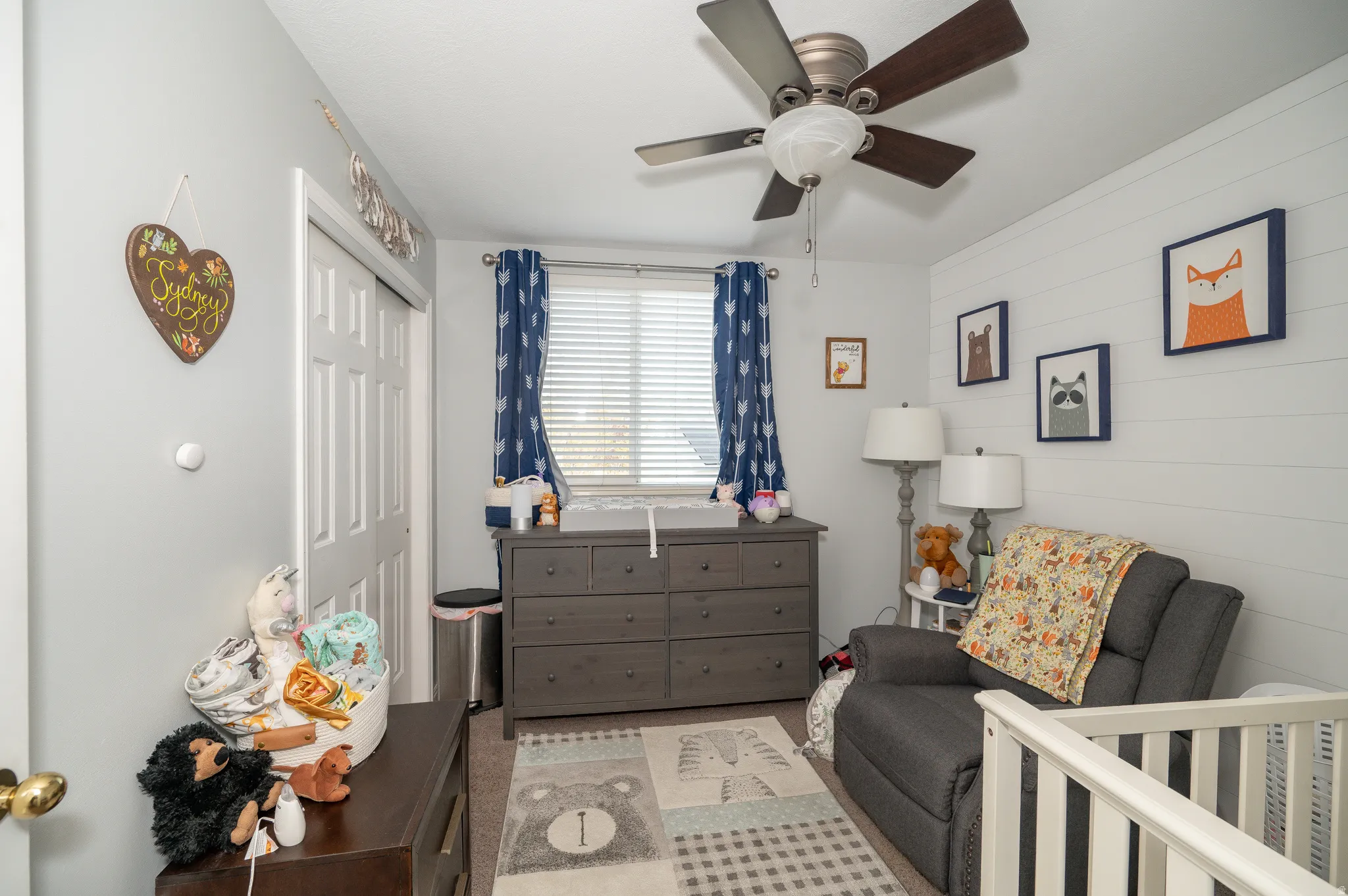 Room featuring a ceiling fan with integrated lighting, a window with blinds, and white shiplap accent wall