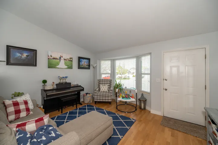 Living room featuring light wood-finish flooring, bay window with blinds, and white paneled entry door