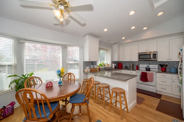 Kitchen featuring white cabinetry, stainless steel microwave, gray subway tile backsplash, and light wood-finish flooring