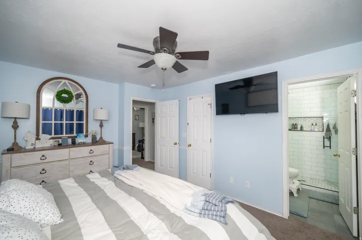 Bedroom featuring a ceiling fan, arched window with white trim, and a wall-mounted television