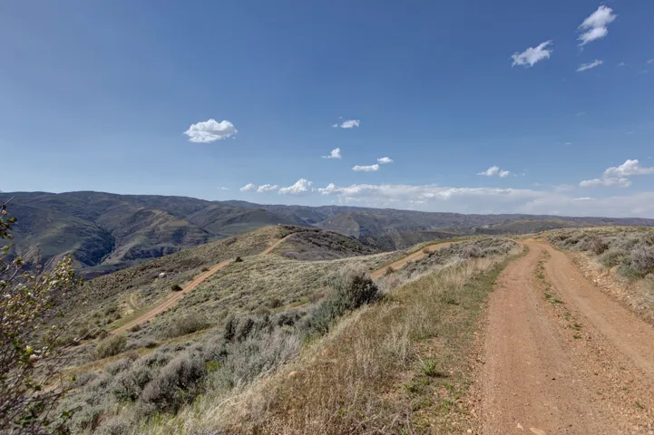 Expansive terrain featuring a winding dirt road, scattered sagebrush, and distant rolling hills