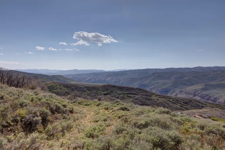 Expansive mountain landscape featuring varied elevations, dense foliage, and distant peaks under a clear sky
