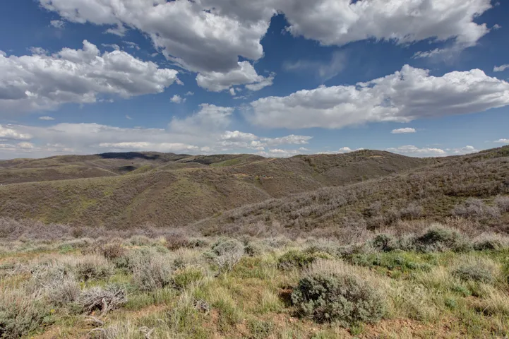 Expansive rolling terrain featuring natural vegetation, distant hills, and a prominent sky with cloud formations
