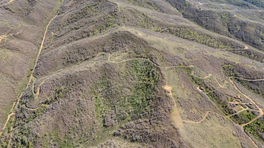 Expansive mountainous terrain featuring multiple winding dirt roads, varied vegetation, and scattered structures