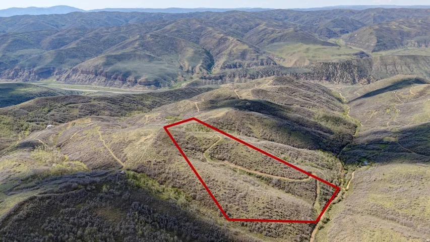Expansive acreage outlined in red, featuring varied terrain and natural vegetation, bordered by rolling hills and distant mountains