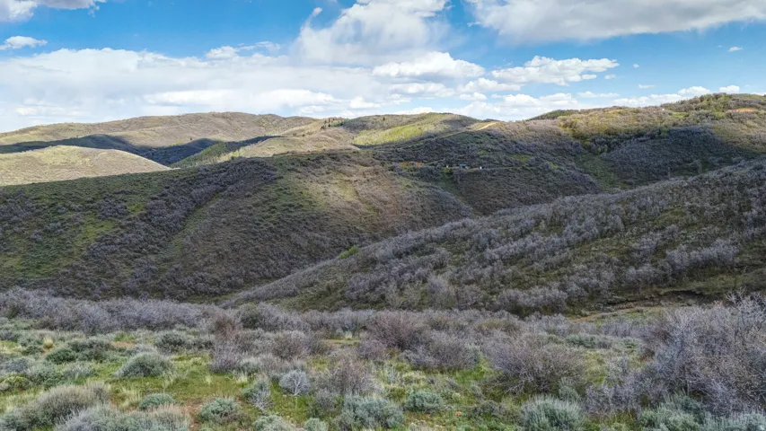 Expansive hilly terrain featuring natural vegetation and distant rolling hills under a partly cloudy sky