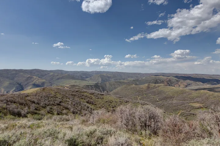 Expansive natural landscape featuring rolling hills and distant mountains under a broad sky with scattered clouds