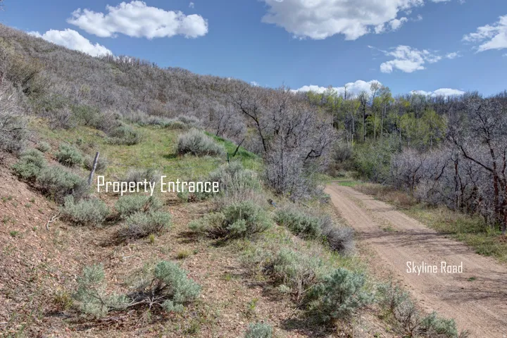 Natural landscape featuring a gradual incline, a visible property entrance, and a dirt road