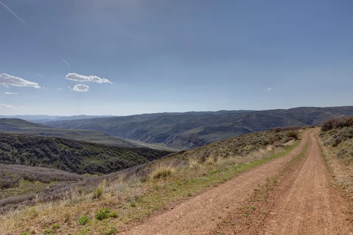 Expansive mountainous landscape featuring a clear sky, distant peaks, and a winding dirt road