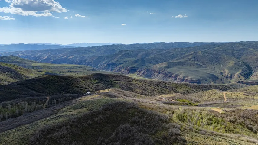 Expansive mountainous landscape featuring distant peaks, rolling hills, and patches of deciduous trees