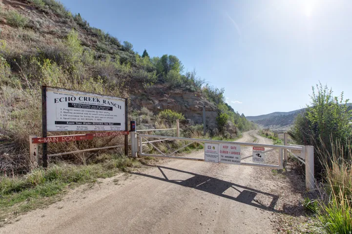 Gated entry to Echo Creek Ranch, featuring a dirt road, signage, and surrounding natural landscape with hills and vegetation
