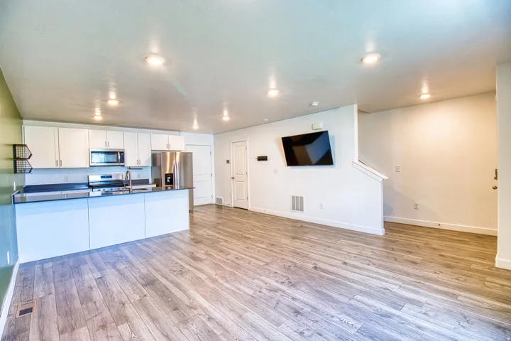 Open-concept living space featuring wood-finish flooring, recessed lighting, and a kitchen with white cabinetry and stainless steel appliances