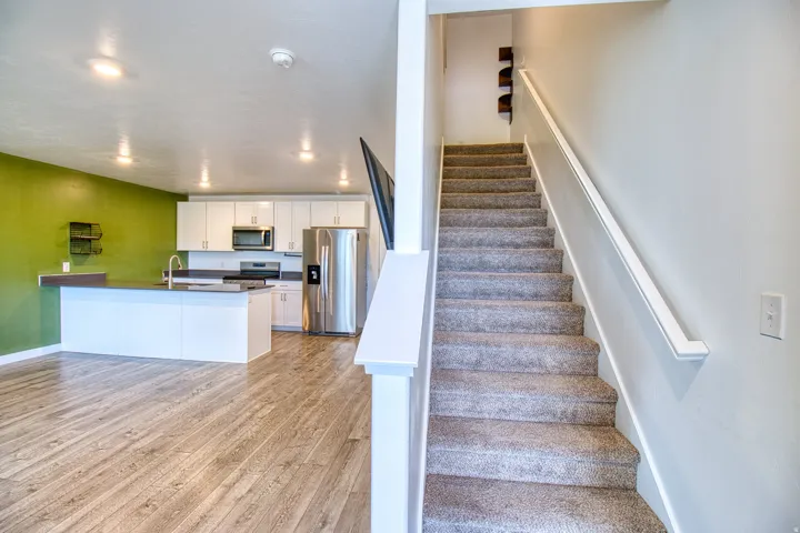 Open-concept living space featuring wood-finish flooring, a kitchen island with sink, white cabinetry, stainless steel appliances, and recessed lighting