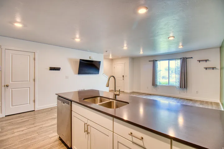 Kitchen island featuring a double-basin stainless steel sink with a high-arc faucet, integrated dishwasher, and white cabinetry with brushed nickel hardware