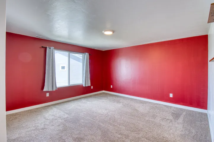 Spacious room featuring broadloom carpeting, a single window with window treatments, a flush mount ceiling light fixture, and contrasting wall colors