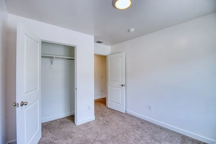 Bedroom space featuring light gray carpet flooring, white painted walls, a built-in closet with double bifold doors, and a flush-mount ceiling light
