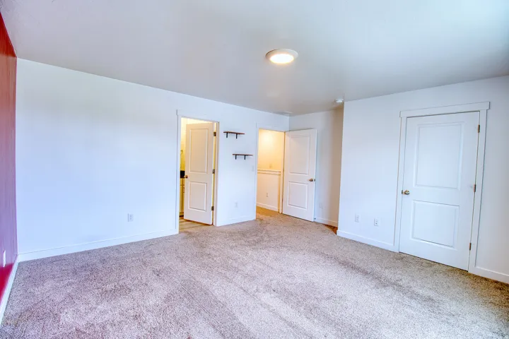 Spacious room featuring neutral carpet, white walls, a single accent wall in a deep red hue, and multiple interior doors with white trim