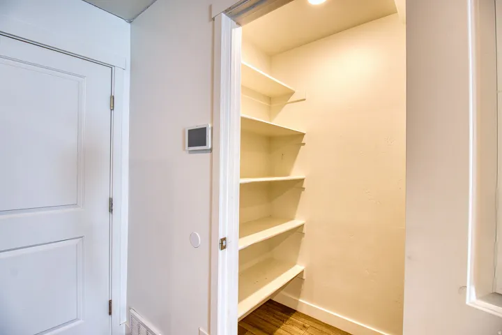 Recessed pantry with five levels of shelving and wood-finish flooring
