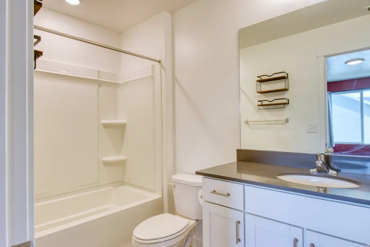 Bathroom featuring a white tub and shower combination, a single vanity with a dark countertop, white shaker-style cabinetry, and a large wall mirror