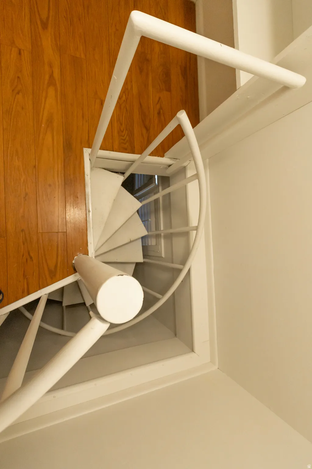 White spiral staircase with an overhead railing, complementing the warm wood-finish flooring