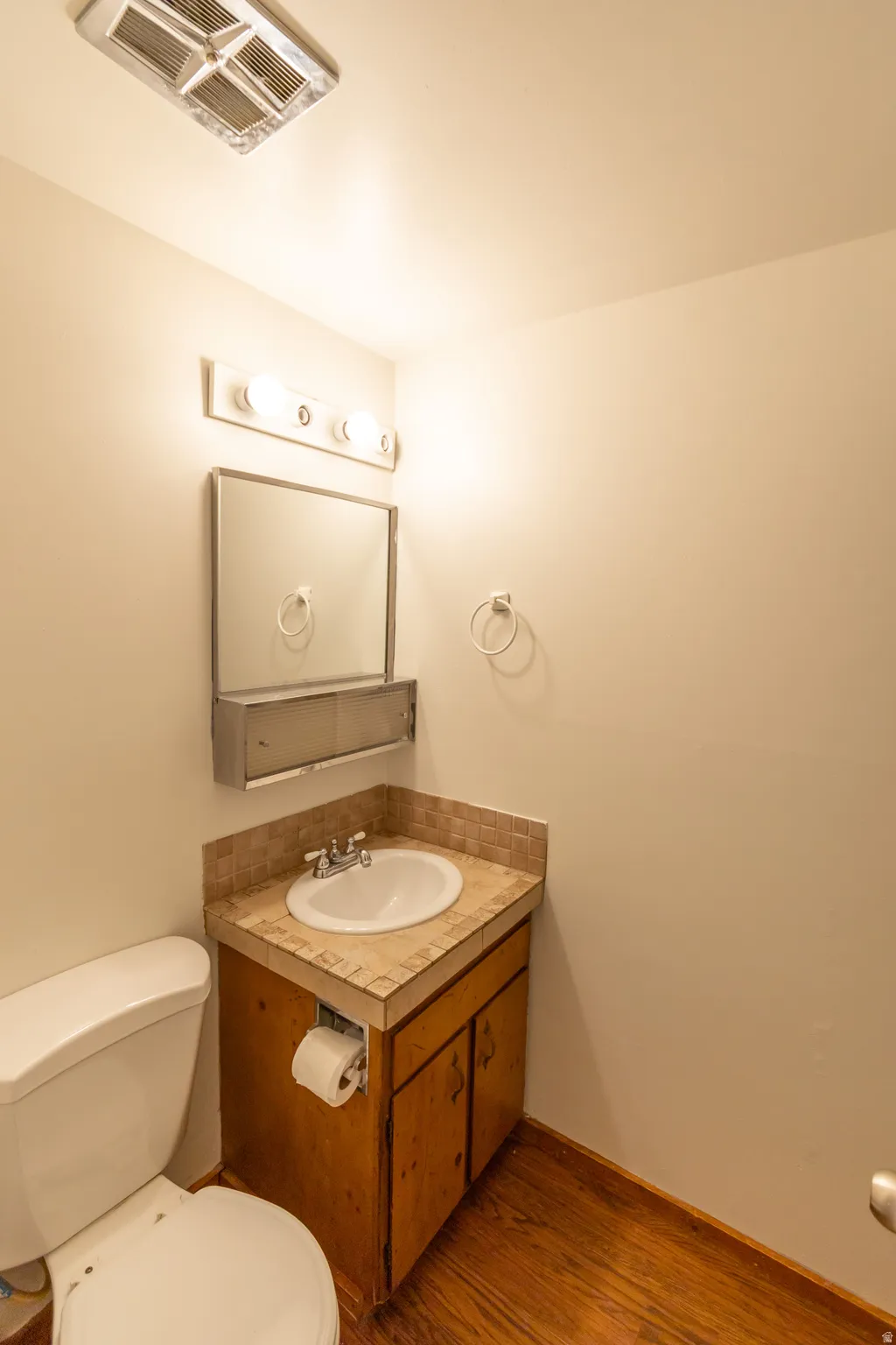 Powder room featuring a wood-finish vanity with a drop-in sink, tiled countertop, and matching tiled backsplash