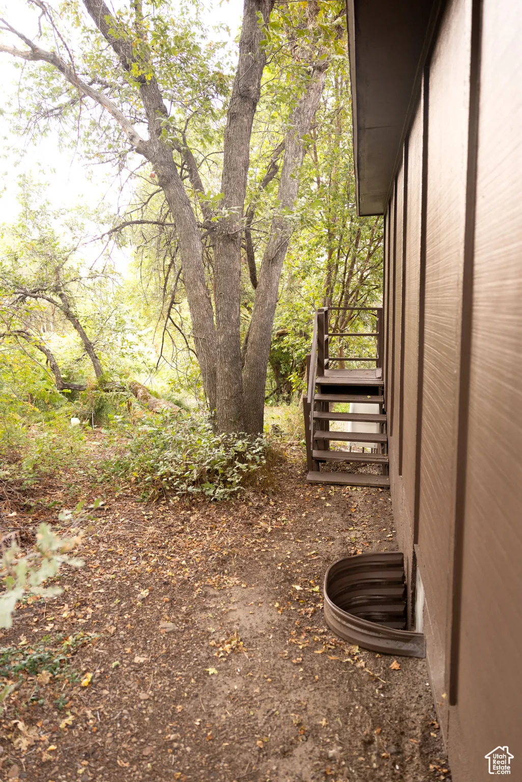 Side exterior with brown vertical siding, a window well, and wooden stairs with railings