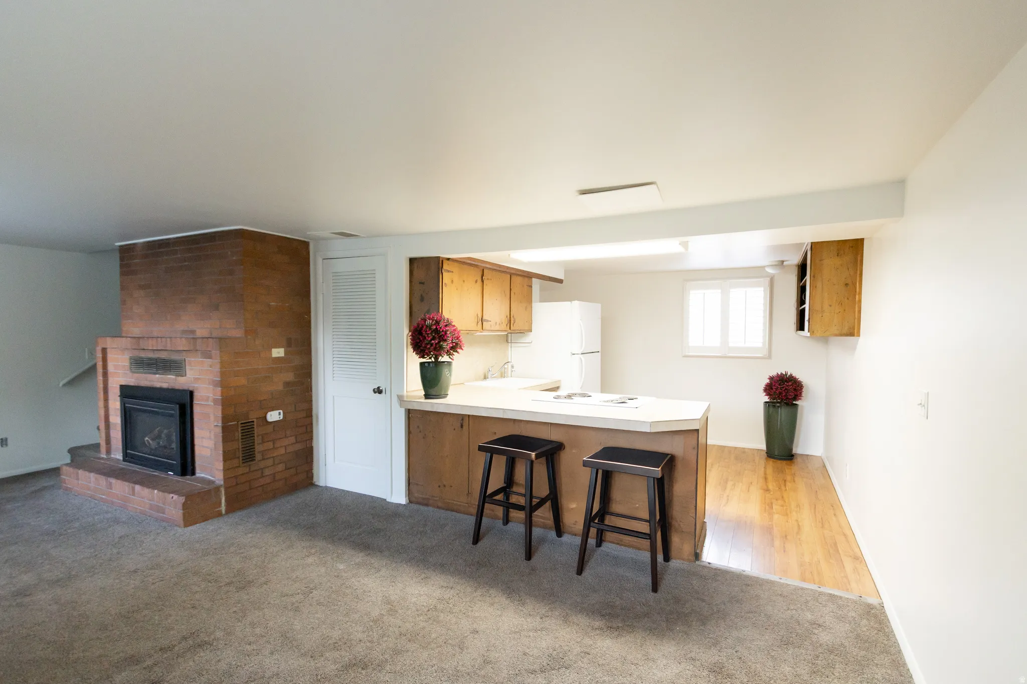 Open living area featuring a brick fireplace with hearth, an integrated kitchen counter with seating, wood-finish flooring, and light wood cabinetry