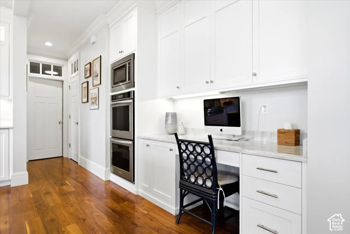 Integrated office nook featuring built-in cabinetry, under-cabinet lighting, a stone countertop, and wood-finish flooring