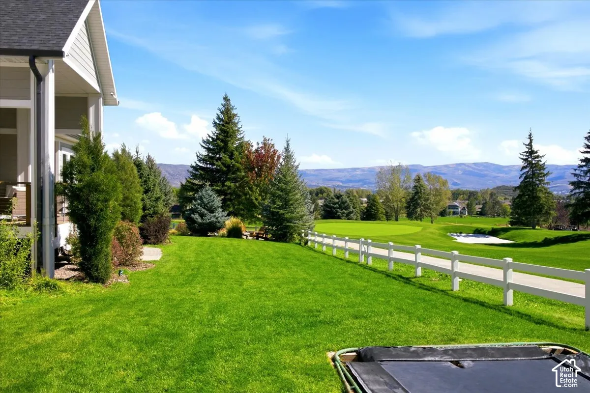 Expansive lawn area with mature trees and a white split-rail fence featuring a gold course view