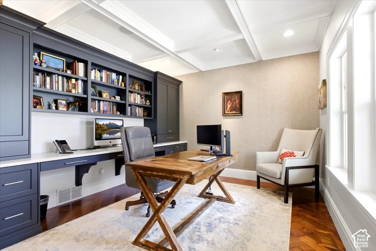 Custom built-in cabinetry with open shelving and closed storage, integrated desk space with a solid surface countertop, coffered ceiling, recessed lighting, and wood-finish flooring