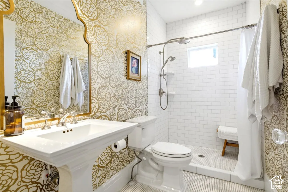 Bathroom featuring gold floral-patterned wallpaper, a white pedestal sink with polished chrome fixtures, and a shower area with white subway tile