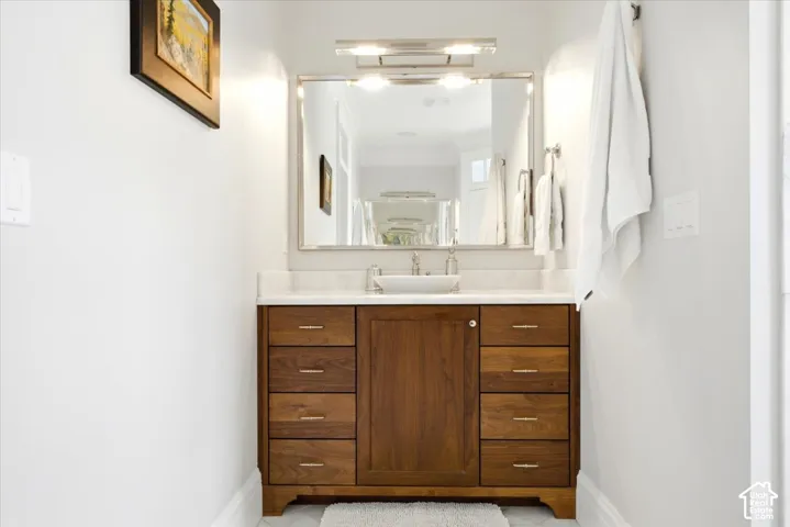 Wood-finish vanity with a vessel sink, stone countertop, and wall-mounted mirror with integrated lighting