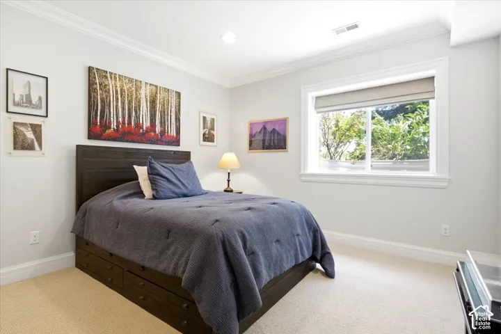Carpeted bedroom featuring a large window with roller shade, crown molding, recessed lighting, and white baseboards