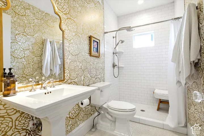 Bathroom featuring gold floral-patterned wallpaper, a white pedestal sink with polished chrome fixtures, and a shower area with white subway tile