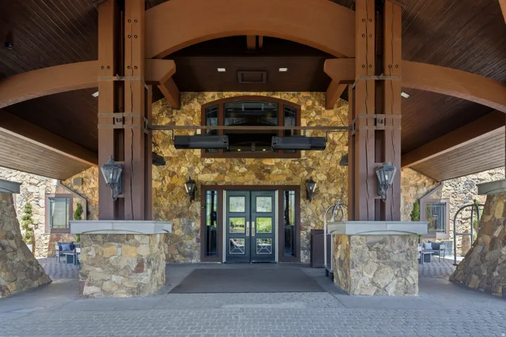 Stone and wood-beam porte-cochère entrance featuring double glass-paneled doors, arched window, and integrated outdoor lighting fixtures