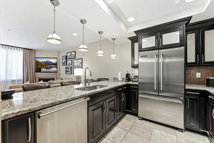 Kitchen featuring granite countertops, dark wood cabinetry, stainless steel appliances, and pendant lighting