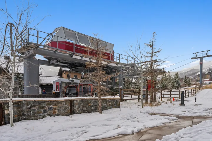 Ski lift station with stone base, supporting multiple ski gondolas, against a backdrop of snow-covered terrain and evergreen trees