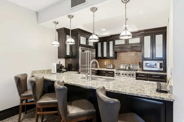 Kitchen featuring dark cabinetry with glass-front uppers, light-toned stone countertops, and a full-size stainless steel range