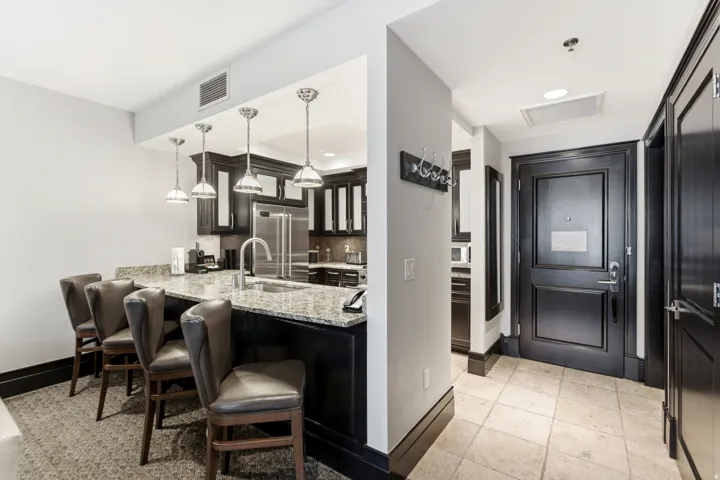 Kitchen with a granite countertop breakfast bar, stainless steel appliances, dark wood cabinetry, and pendant lighting