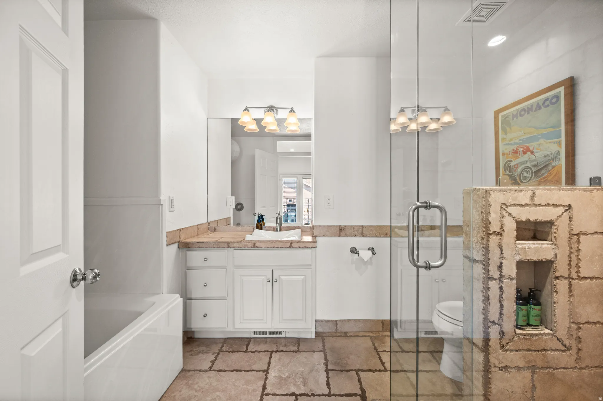 Primary bathroom featuring a glass-enclosed shower, stone-finish countertop and separate jetted tub