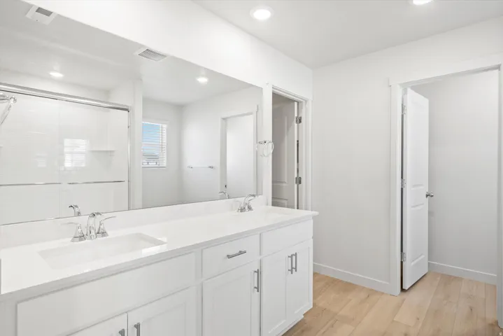 Bathroom featuring a double vanity with white cabinetry and integrated sinks, a large wall-mounted mirror, and wood-finish flooring