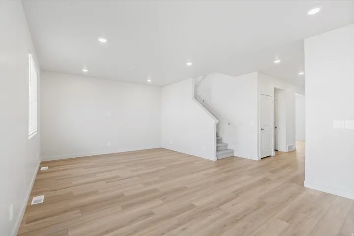 Expansive living area featuring light wood-finish flooring, recessed lighting, and a neutral white color palette