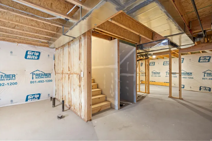 Unfinished basement presenting framed walls, exposed ductwork, a concrete floor, and a wooden staircase