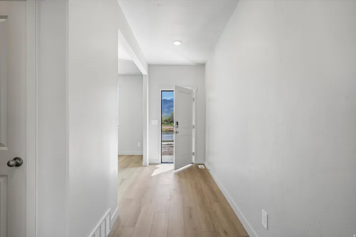 Bright entryway featuring light wood-finish flooring, crisp white walls, recessed lighting, and a white paneled door