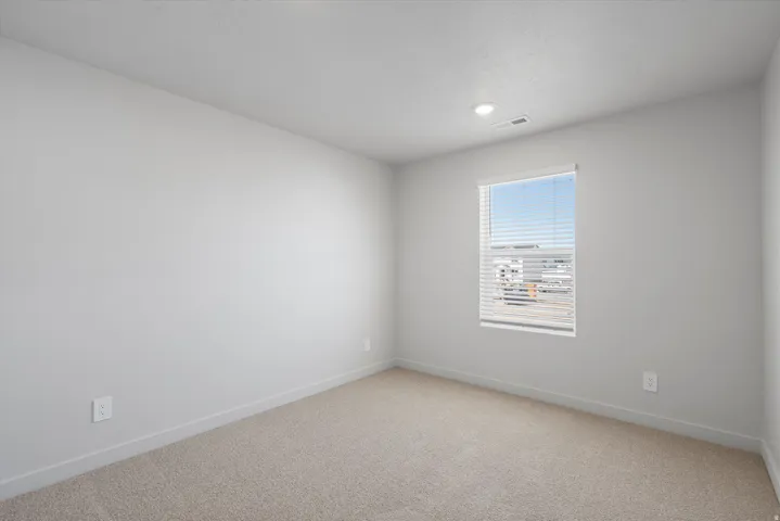 Bright interior room featuring a single window with blinds, recessed lighting, neutral wall paint, and plush carpeting