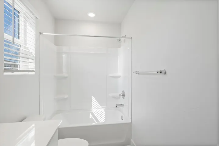 Bright bathroom featuring a white tub and shower combination with integrated shelving, chrome fixtures, and a recessed ceiling light