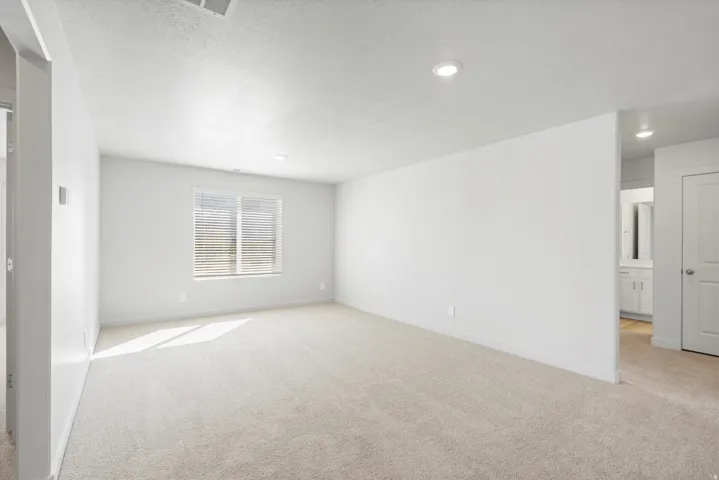 Spacious carpeted room featuring a large window with blinds, recessed lighting, and neutral wall finishes